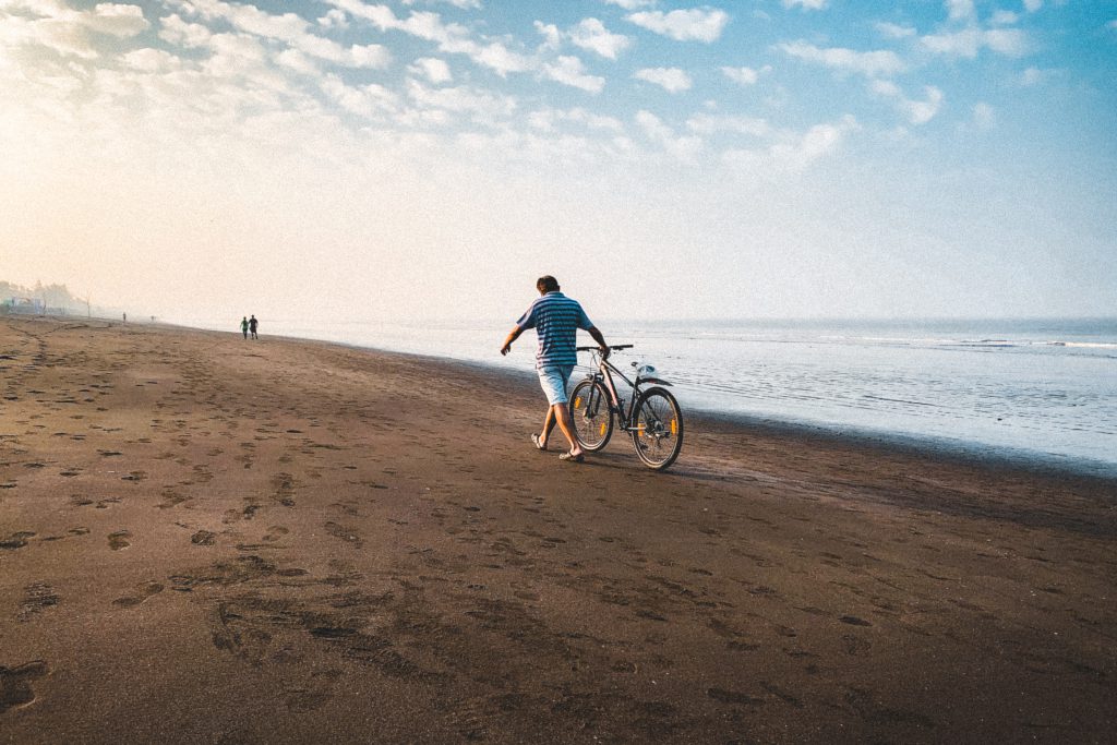 man walking bike on the beach