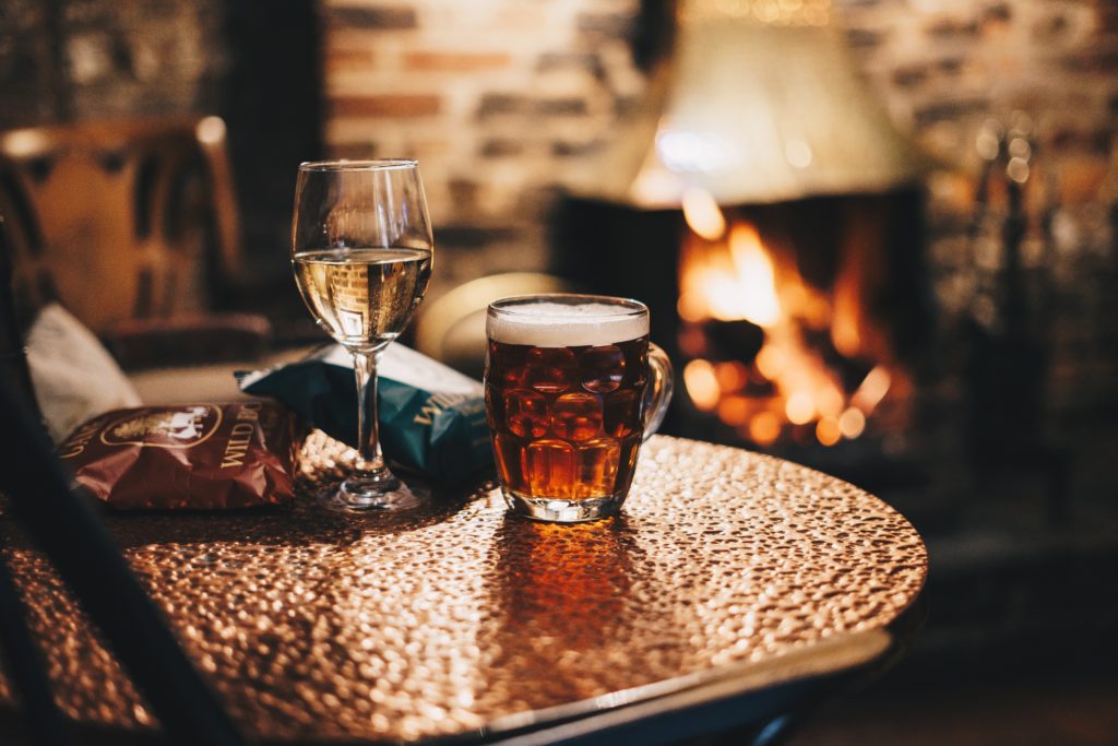 pint and a glass of wine on a pub table in front of a wood burner